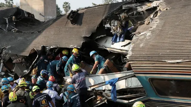 People gathering around a large hole on the stop of an overturned train