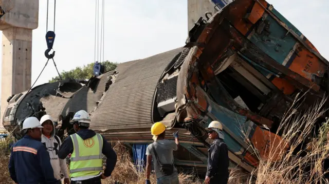 Men in helmets standing in front of an overturned train