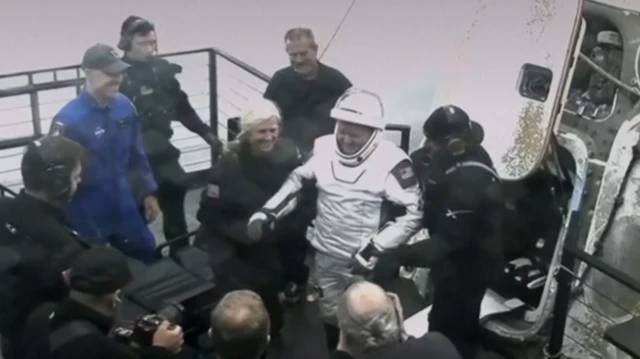 People surround astronaut leaving space craft