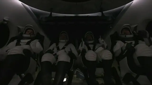 The four astronauts inside the Dragon Endeavour sat in a line. They are wearing white space suits and strapped in by black straps
