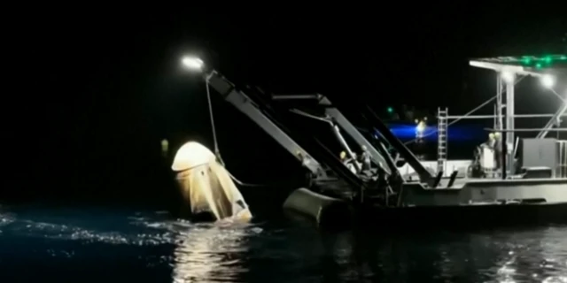 Dragon Endeavour capsule being pulled out of the water by a rope onto the back of a boat.