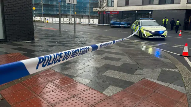 A police vehicle and a cordon on a street in Plymouth. Police officers are standing next to a parked police car.