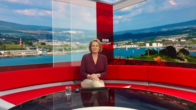 Victoria Graham sitting down on a red sofa in a news studio.