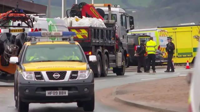 A coastguard vehicle in front of a lorry with sandbags.