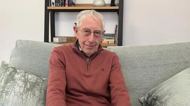 An older man with short, white hair and a brown quarter-zip jumper.