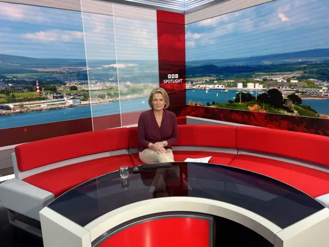 A picture of Victoria sat on a sofa in the Spotlight newsroom. The sofa is red in colour with a lit up background.
