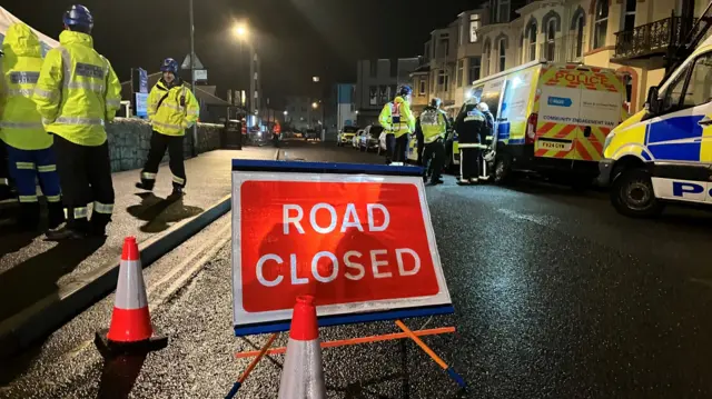 Emergency services and other workers by vehicles behind a road closed sign