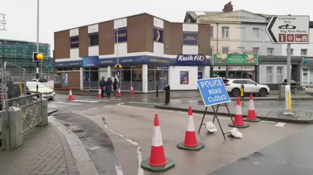 A view down a road in Plymouth showing a police road closed sign and plastic traffic cones.