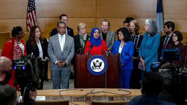 A large groups of Democratic lawmakers speaks in front of a podium