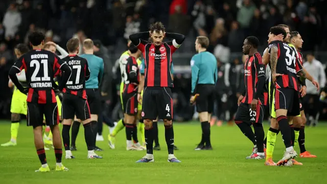 Eintracht Frankfurt players look on in confusion as they concede a late equaliser against Borussia Dortmund. They are wearing black and red striped kits.