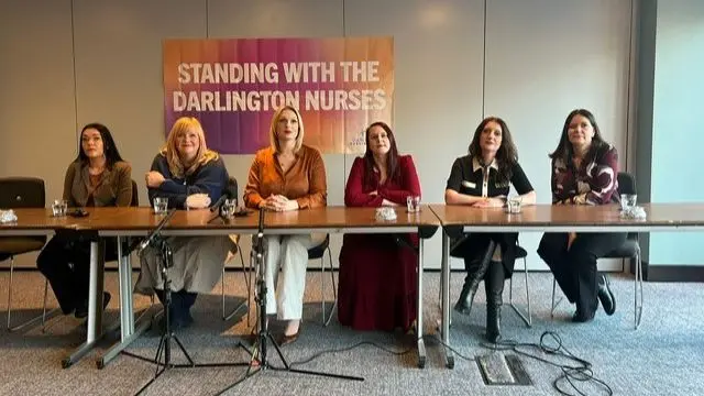 Six women sit in chairs behind a table