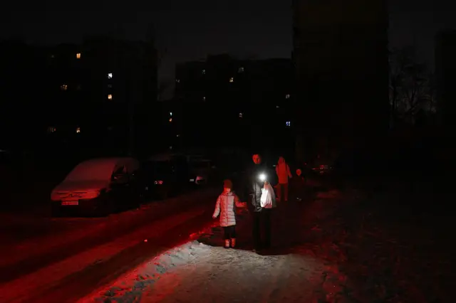 People walk along a dark street during a power outage in Kyiv holding up a phone for light