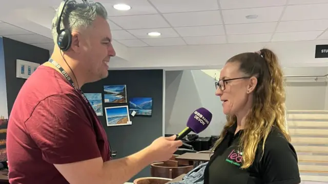 Two people talking, one is wearing headphone and holding a microphone