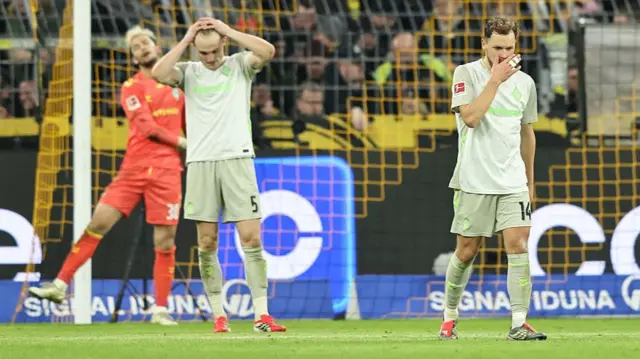 Werder Bremen players look upset as they lose another match. They are wearing their grey and green away kit.