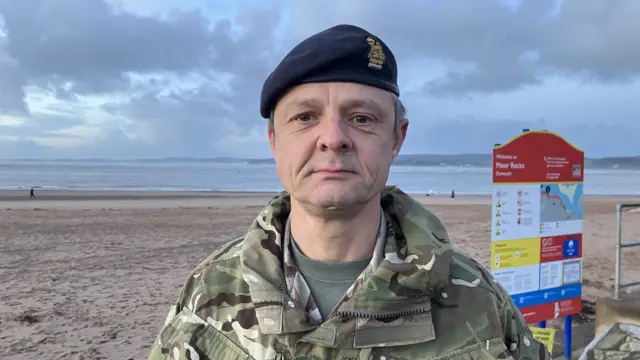 British Army Colonel Darren Fisher stood on the beach wearing army uniform.