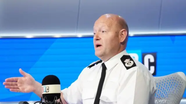 Craig Guildford gestures as he speaks into a microphone at a radio desk during a phone-in on LBC