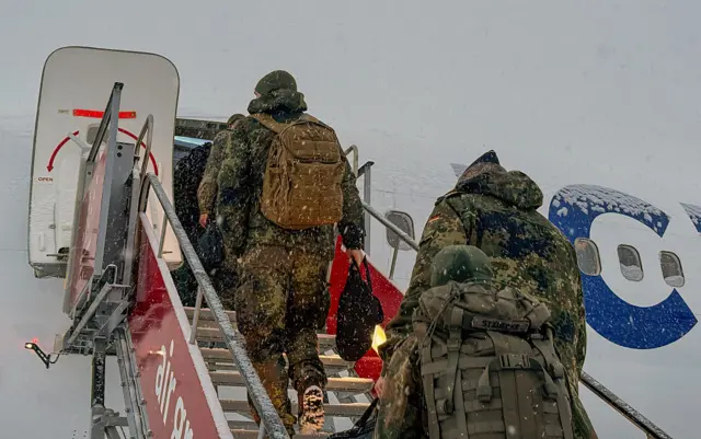 Three members of the German armed forces in military fatigues board a plane at Nuuk airport under the snow