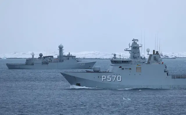 Two Danish ships pass each other on the sea off the coast of Nuuk. In the far off background, are snow-covered mountains