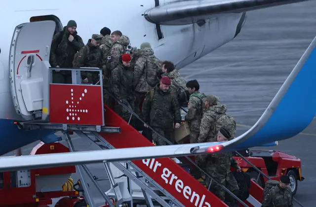 A group of German soldiers disembark from a Air Greenland plane, while another group of soldiers walks up into the plane. They're all wearing military uniforms