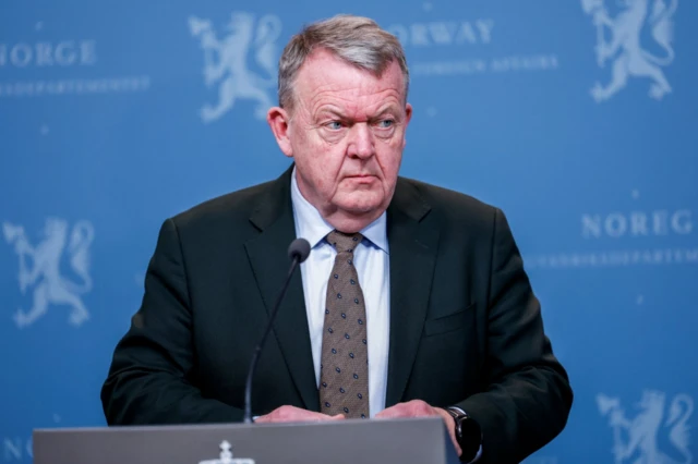 Danish foreign minister Lars Løkke Rasmussen in a black suit, white shirt and tie stands behind a lectern during a press conference