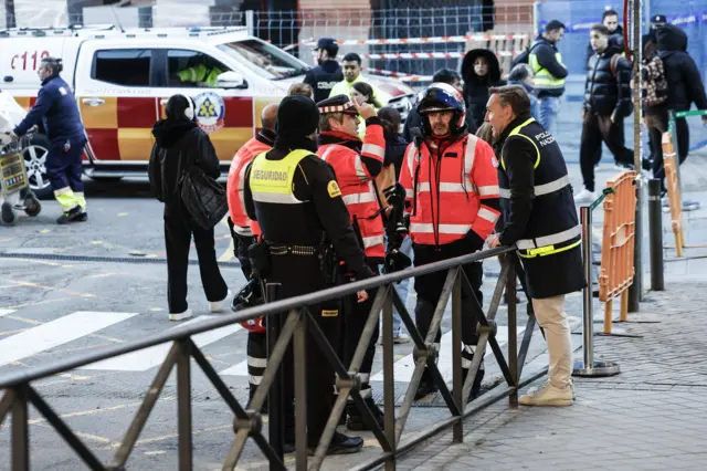 People in hi vis jackets gather and chat outside a train station with an emergency vehicle behind.