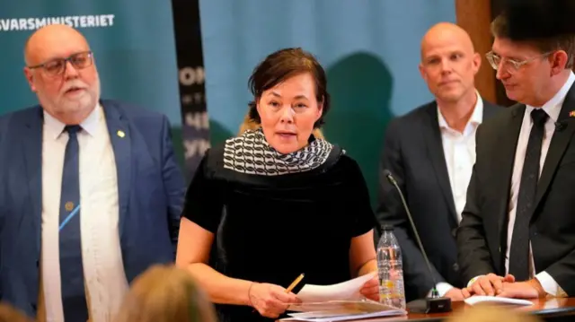A group of four people stand in a group while a woman reads from a piece of paper