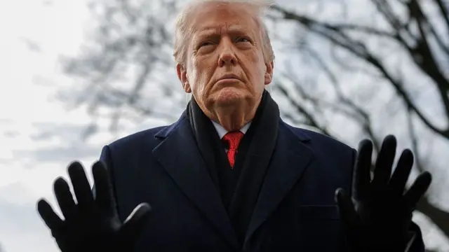 Trump standing outdoors in a coat, scarf and gloves holding both hands outstretched