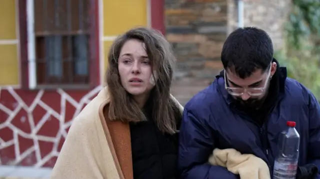 Ana, a young woman who survived the crash, has her arm linked with a man's with a blanket around her shoulders.