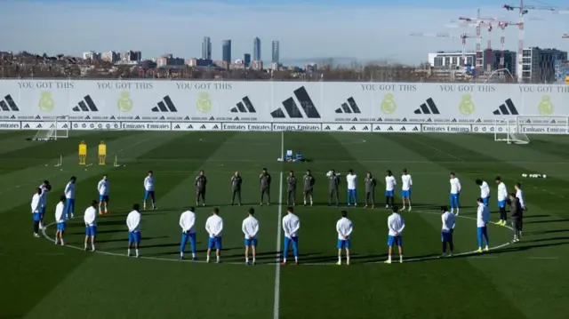 Football players stand in a circle on a training pitch with the Madrid skyline in the background