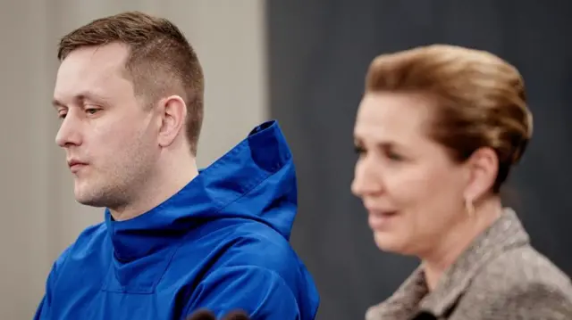 A man in a blue coat stands next to a woman in a brown jacket