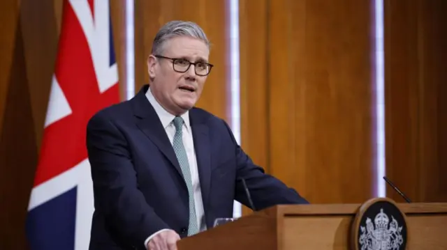 Keir Starmer stands at a podium in front of a Union Jack flag