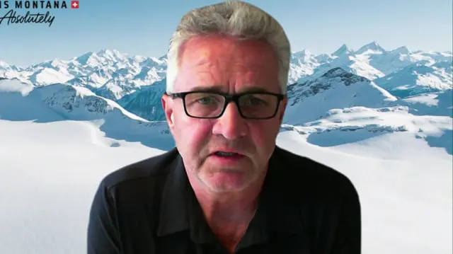 Bruno Huggler looks to camera as he speaks - a picture of snowy mountains makes up the background behind him