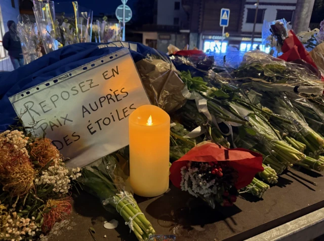 Flowers laid next to a candle, a note in french says "rest in peace among the stars"