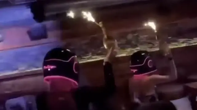 A screengrab from the promotional video showing two women in helmets carrying bottles with sparklers attached to the necks