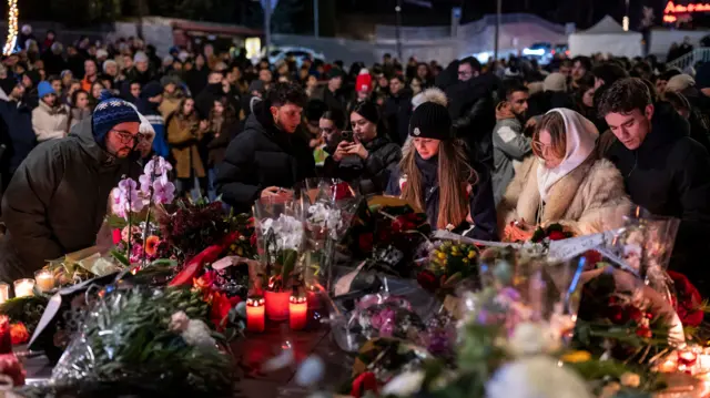 Several hundred mourners gather to lay down flowers and light candles to remember the victims of the fire at the "Le Constellation" bar