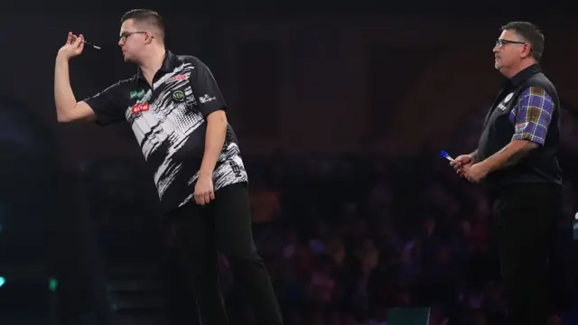 Gian van Veen throws a dart as Gary Anderson looks on