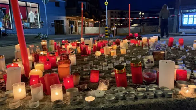 Red and white candles, many still lit, on the side of the road - the morning is still dark