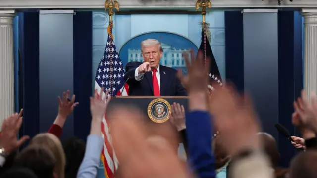 Donald Trump raises his left arm as he points to members of the media at a press briefing at the White House
