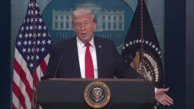 Donald Trump with his right arm stretched out to his side as he speaks to the media from the White House briefing room