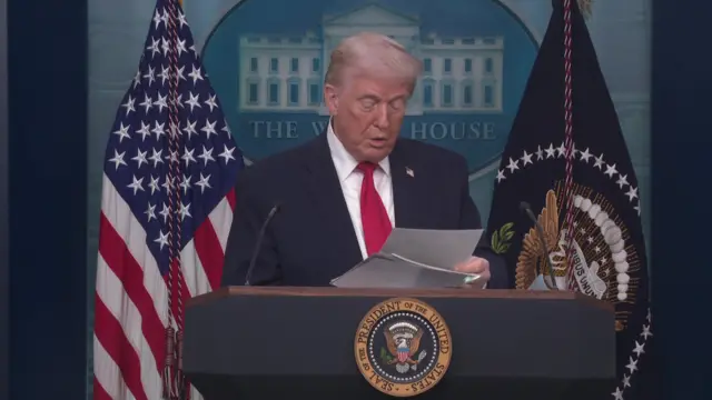 Donald Trump looks down at a binder of files as he speaks to the media in the White House briefing room