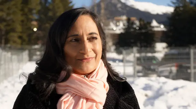 Canada's foreign minister, who has long dark hair, is standing in front of a snowy mountainous background