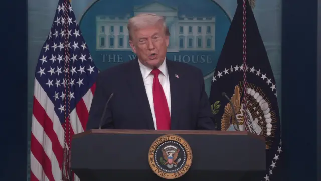 Donald Trump standing behind a podium next to the American flag as he speaks to the media