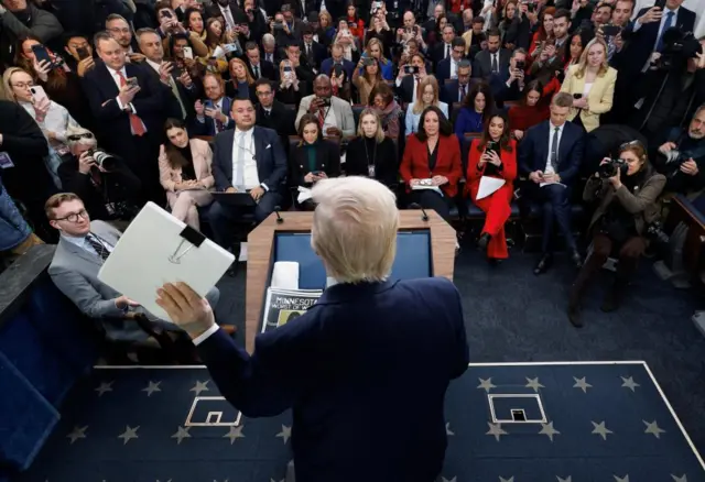 President Donald Trump stands before a throng of reporters in the briefing room of the White House