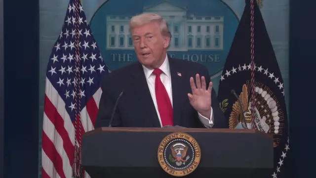 Trump holds up his hand as he speaks to the media in the White House briefing room