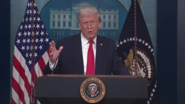 Donald Trump raises his left hand in the air as he speaks to the media from the White House briefing room