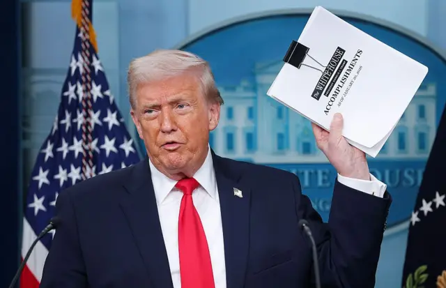 US President Donald Trump holds up a file titled “White House Accomplishments” in the press briefing room at the White House.