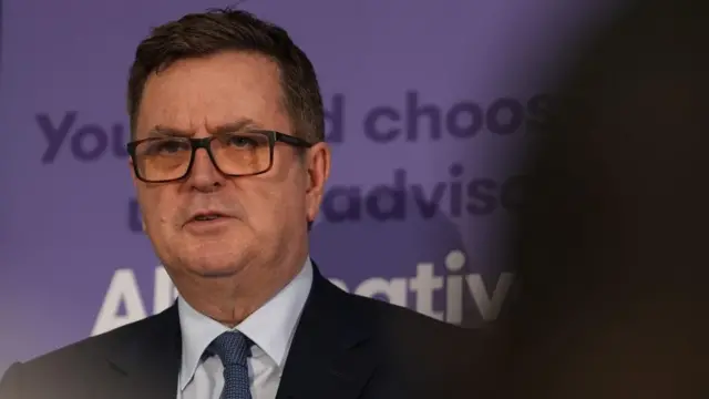 Mel Stride stands in front of a purple sign