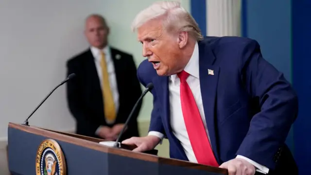 Trump grips on to the podium while delivering his briefing in the White House press room