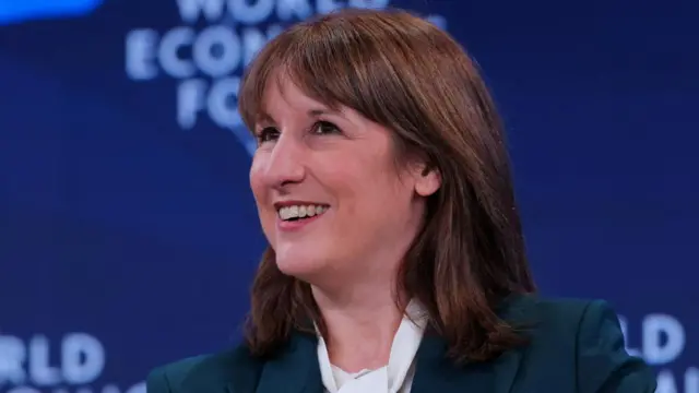 Reeves smiling in front of 'World Economic Forum' advertising