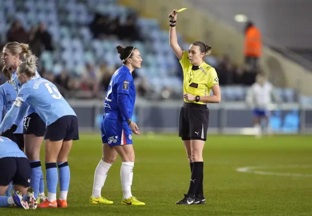 Referee Phoebe Cross shows a yellow card to Chelsea's Lucy Bronze